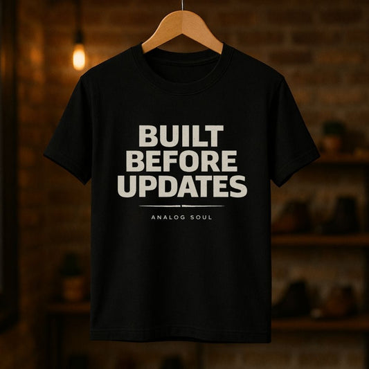 Black ‘Built Before Updates’ t-shirt hanging on wooden hanger, minimalist analog soul typography