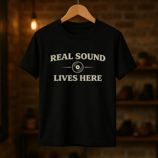 Black t-shirt with 'Real Sound Lives Here' text on a wooden hanger against a dark background