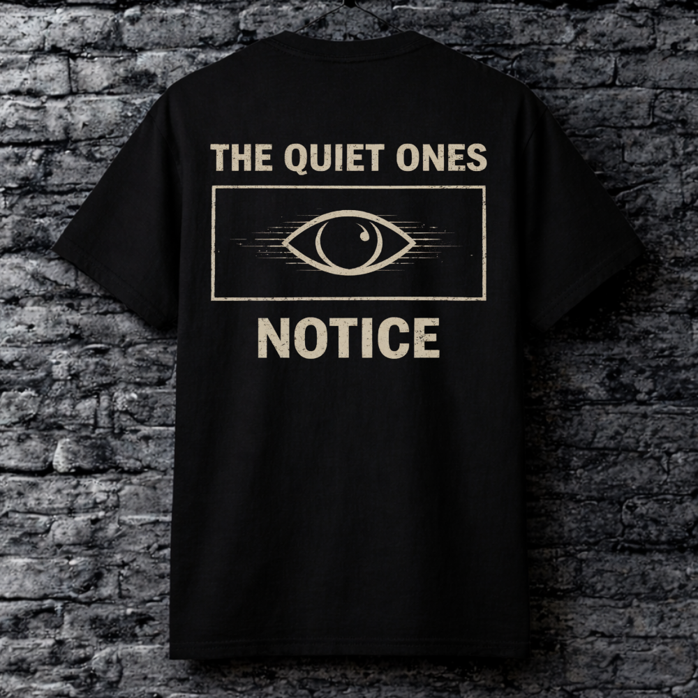 Black t-shirt with 'The Quiet Ones Notice' text and eye graphic on a brick wall background