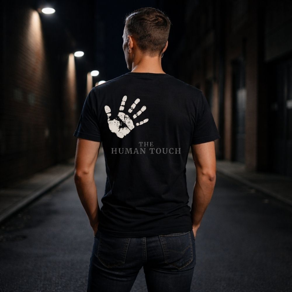 Person wearing a black t-shirt with 'The Human Touch' design on the back in a dark alley.
