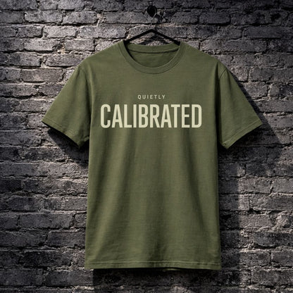 Green t-shirt with 'QUIETLY CALIBRATED' text on a brick wall background