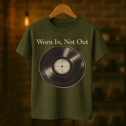 Green t-shirt with vinyl record graphic and 'Worn In, Not Out' text on a hanger against a dark background.