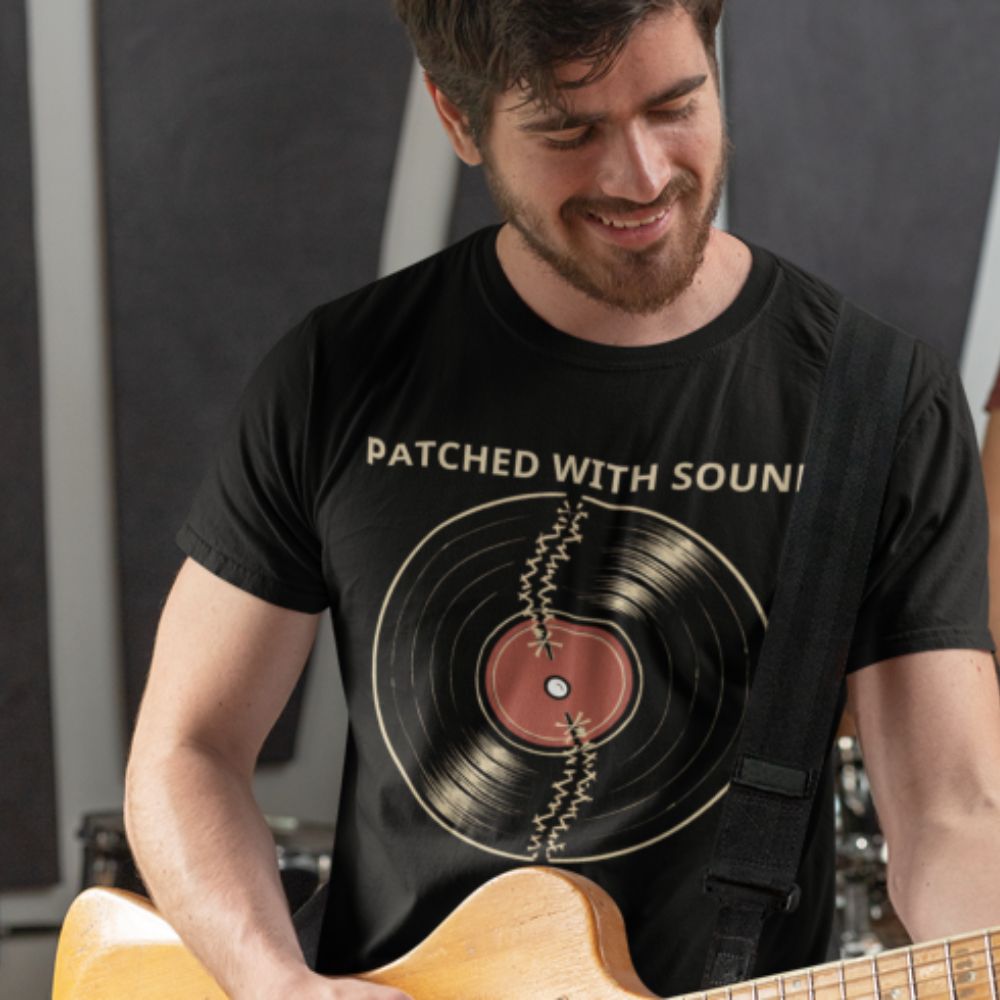 Man wearing a black t-shirt with a vinyl record design and text, holding a guitar.