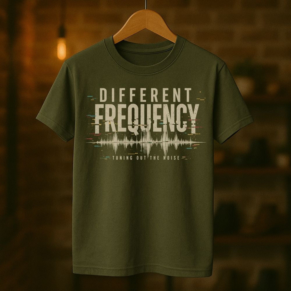 Green t-shirt with 'Different Frequency' text on a wooden hanger against a blurred background