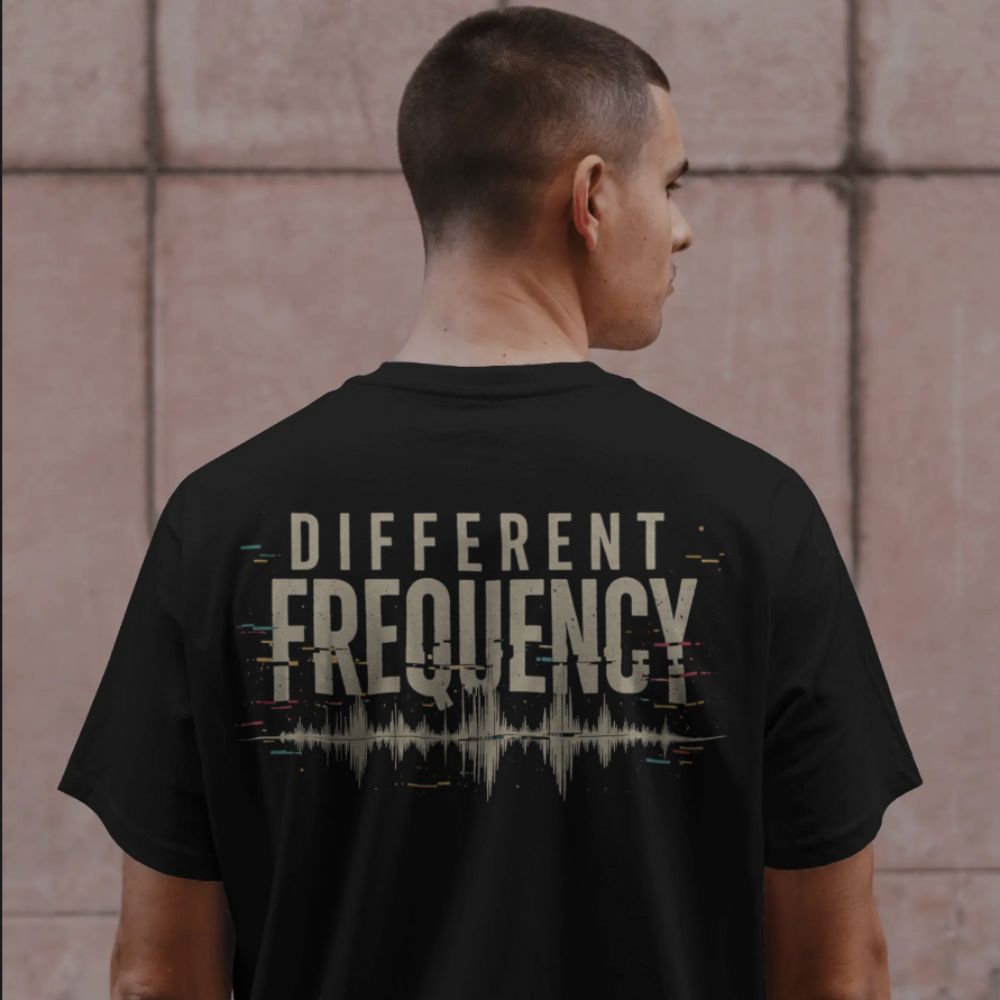 Person wearing a black t-shirt with 'DIFFERENT FREQUENCY' text on the back, standing against a textured wall.