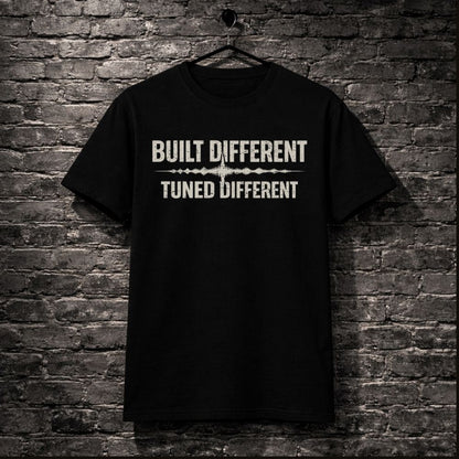 Black t-shirt with 'Built Different Tuned Different' text on a brick wall background