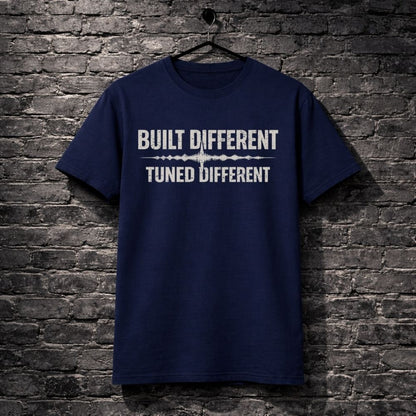 Navy blue t-shirt with 'Built Different Tuned Different' text on a brick wall background