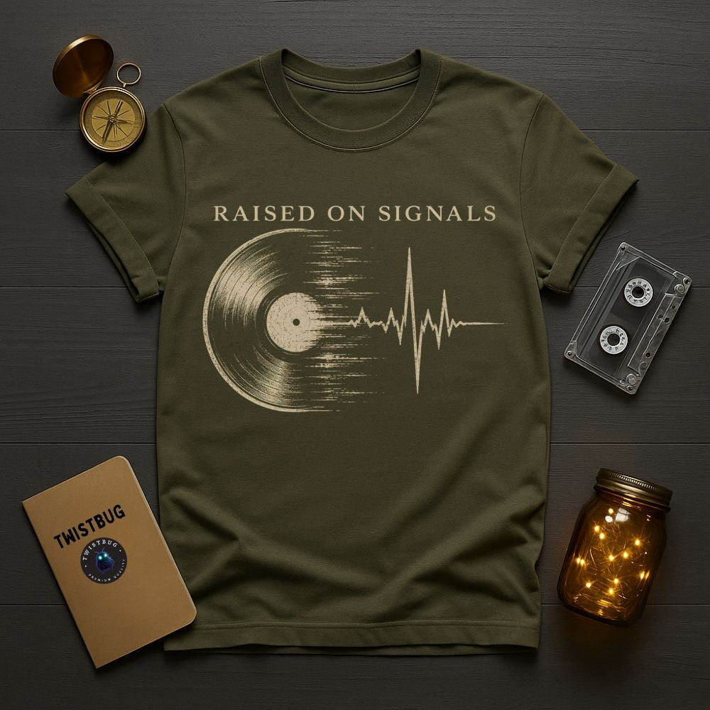 Green t-shirt with 'Raised on Signals' design on a wooden surface with vintage items.