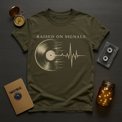 Green t-shirt with 'Raised on Signals' design on a wooden surface with vintage items.