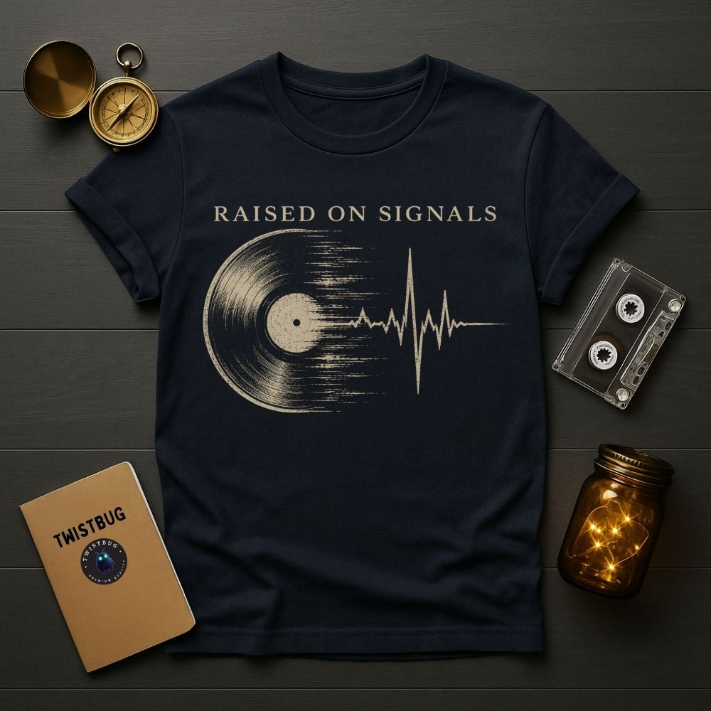 Black t-shirt with 'Raised on Signals' design on a wooden surface with vintage items.