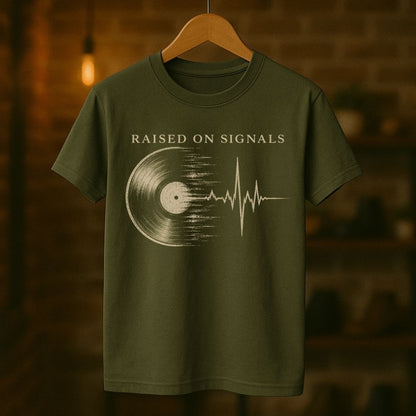 Green t-shirt with 'Raised on Signals' design on a wooden hanger against a blurred background