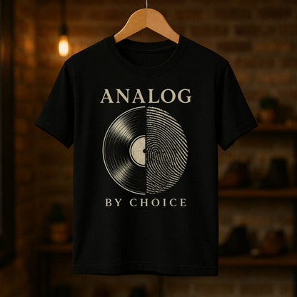 Black t-shirt with vinyl record design and 'Analog by Choice' text on a wooden hanger against a brick wall.