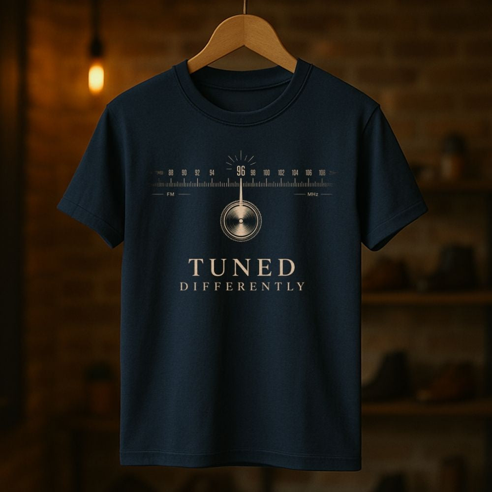 Navy blue t-shirt with 'Tuned Differently' design on a wooden hanger against a dark background
