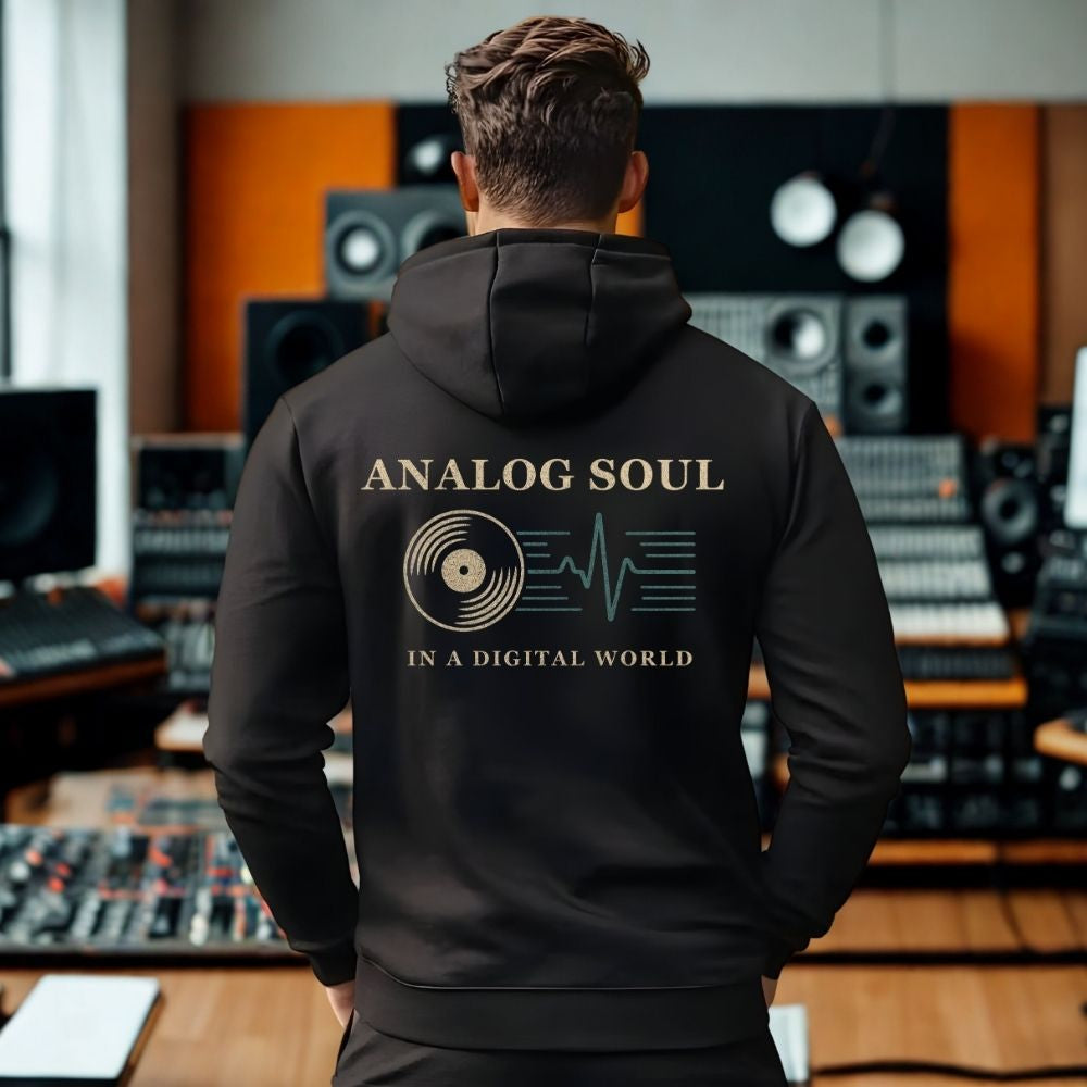 Person wearing a black hoodie with 'Analog Soul in a Digital World' text in a music studio.