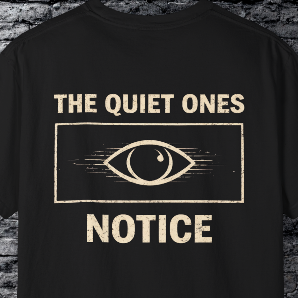 Black t-shirt with 'The Quiet Ones Notice' text and eye graphic on a brick wall background