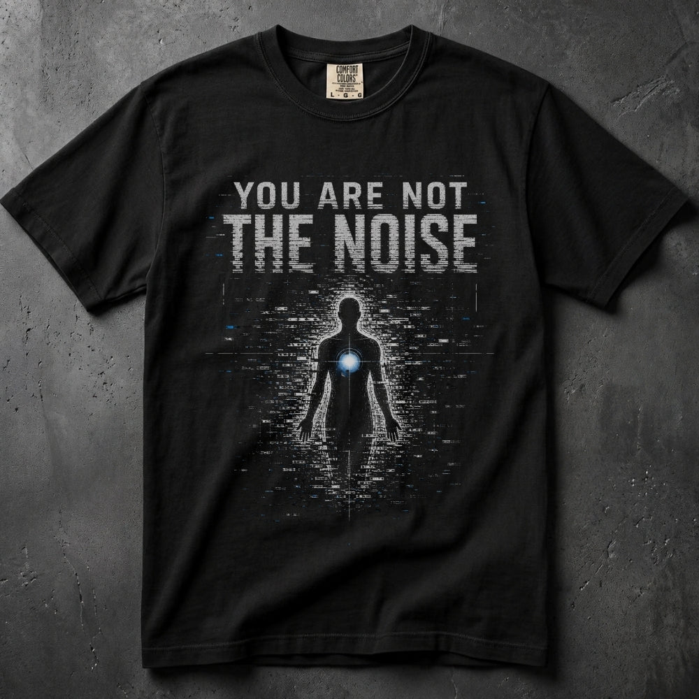A black graphic t-shirt laid flat on a textured dark gray background. The shirt features a distressed white text print reading 'YOU ARE NOT THE NOISE' above a digital glitch-style silhouette of a human figure with a glowing blue light in the chest area.