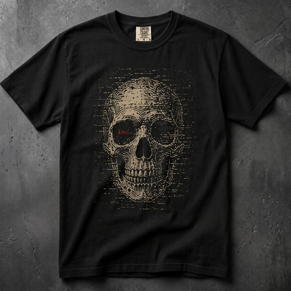 A black short-sleeve crewneck t-shirt featuring a large distressed beige skull graphic on the front, with a small red 'LIVE' text detail inside the left eye socket. The shirt is laid flat on a textured dark gray concrete surface.