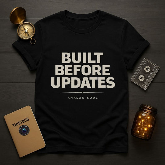 Black t-shirt with ‘Built Before Updates’ text design, analog soul minimalist graphic, flat lay on dark surface.