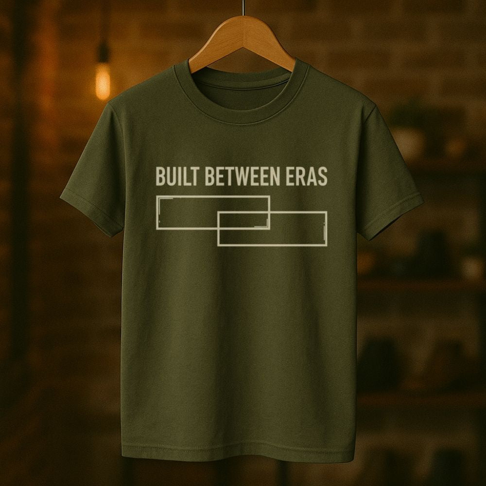 Green t-shirt with 'Built Between Eras' text on a wooden hanger against a blurred background