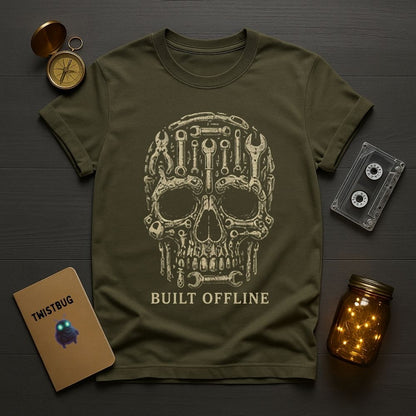 Green t-shirt with mechanical skull design and 'Built Offline' text, placed on a wooden surface with a pocket watch, cassette tape, and jar.