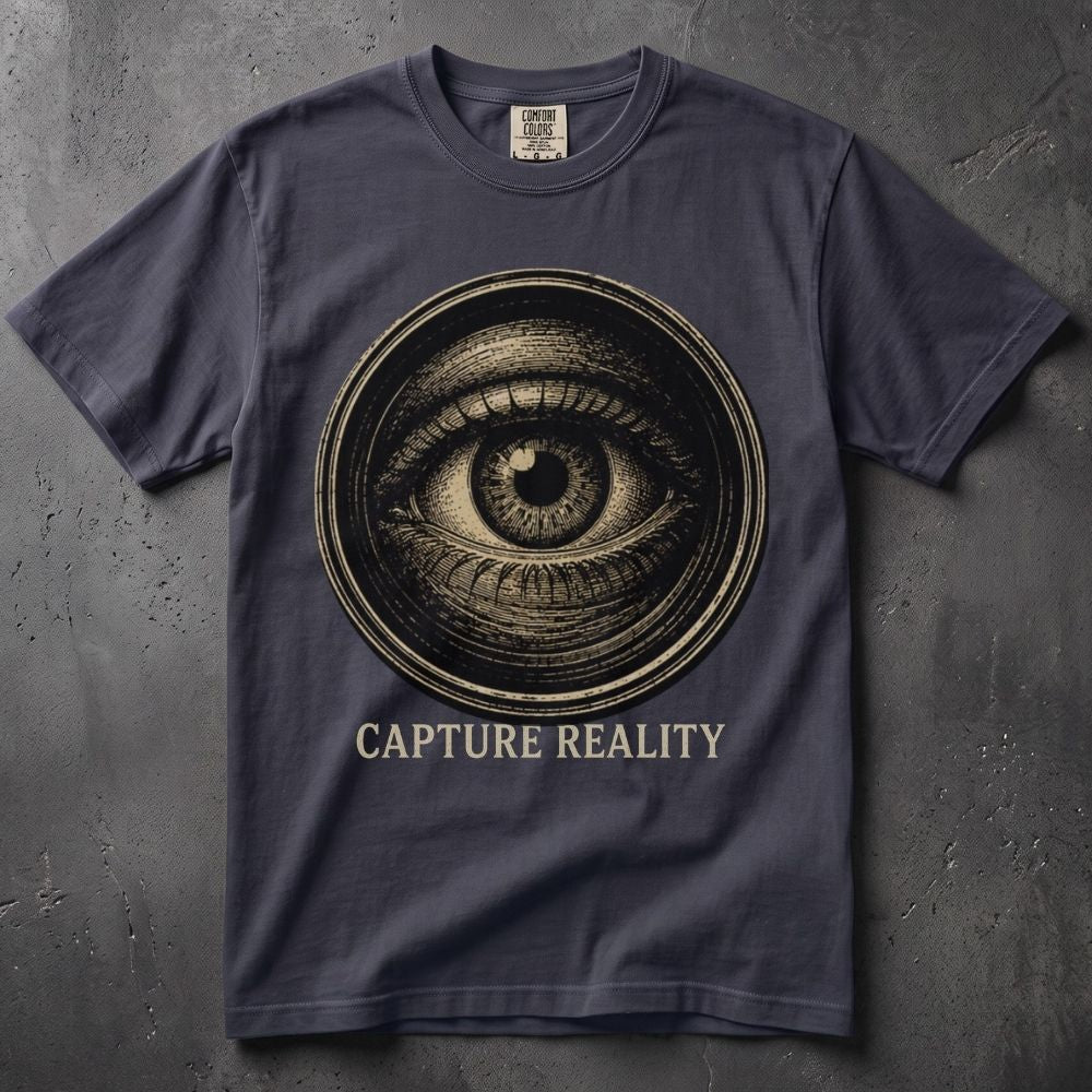 A dark navy blue t-shirt with a circular all-seeing eye graphic in beige and the text 'CAPTURE REALITY' printed below it, displayed flat against a textured gray background.