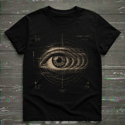 A black short-sleeve crewneck t-shirt featuring a detailed beige graphic of a human eye with technical blueprint markings and the text 'CHANNEL BLEED' on the chest, displayed flat on a dark wood plank background.