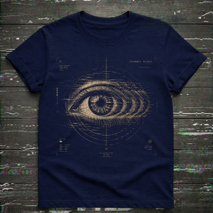 A navy blue short-sleeve t-shirt with a detailed beige blueprint-style eye graphic on the front, laid flat on a dark rustic wooden background.