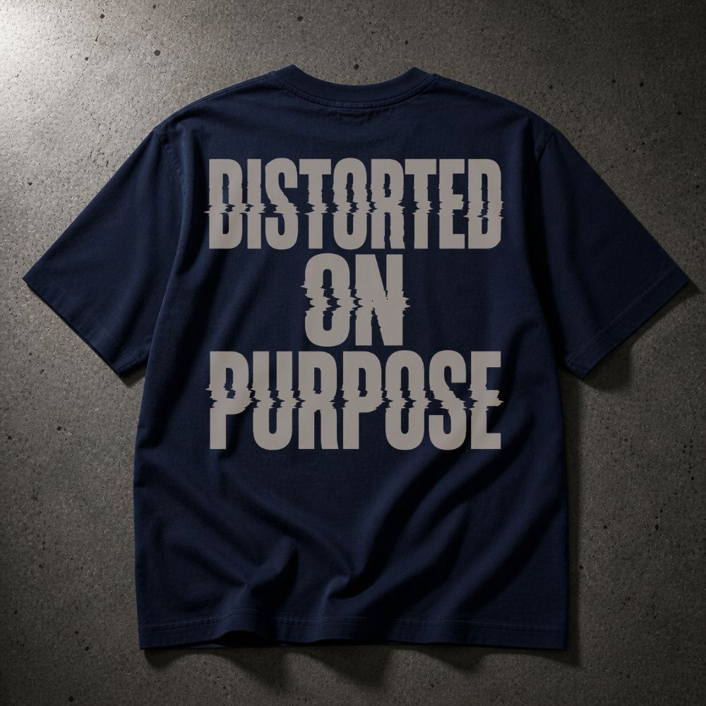 A navy blue short-sleeve t-shirt with the phrase 'DISTORTED ON PURPOSE' printed in a large, distressed light gray font across the back, laid flat on a dark textured concrete surface.