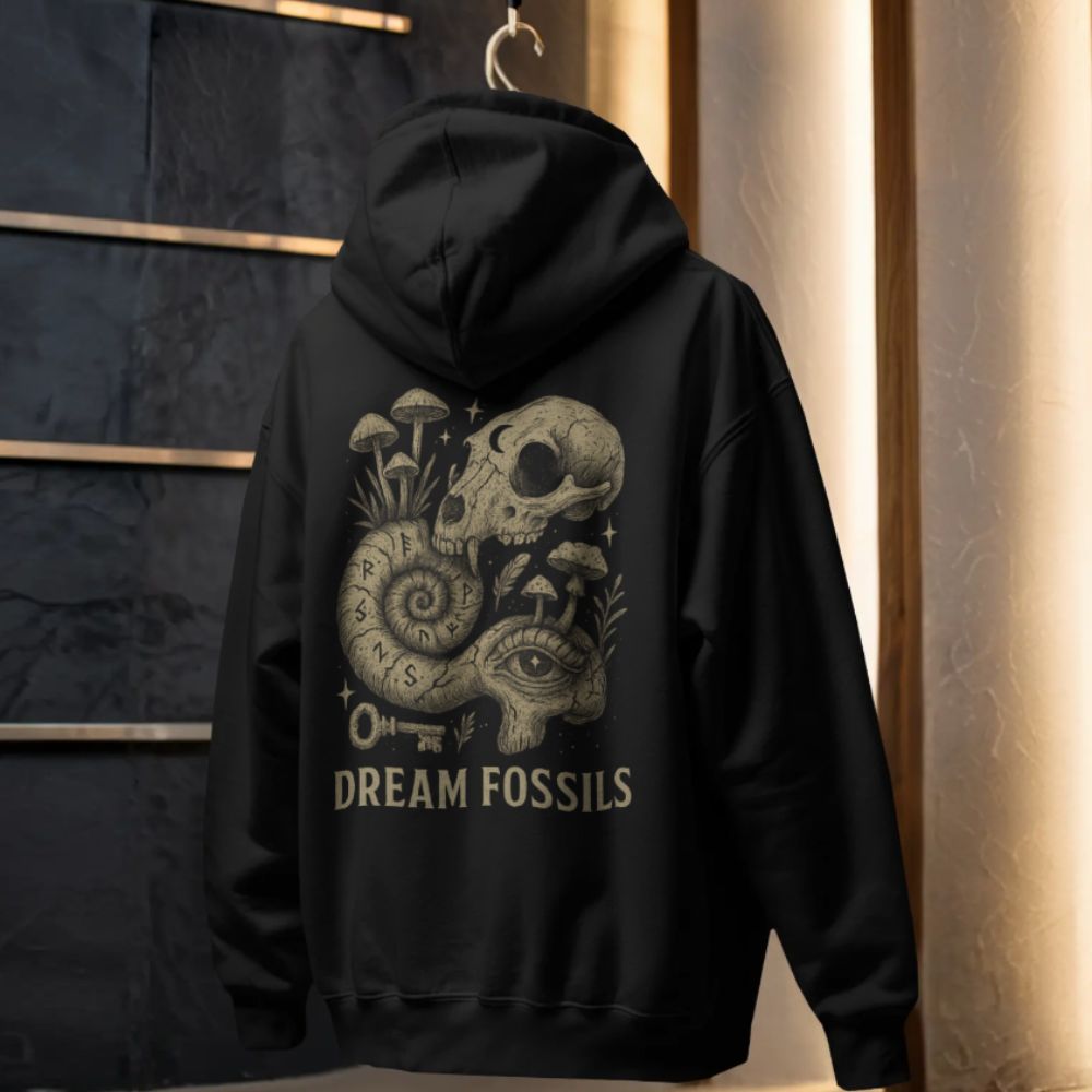 Black hoodie featuring the “Dream Fossils” back design with a skull, spiral snail shell, mushrooms, and symbolic elements, photographed in a studio setting