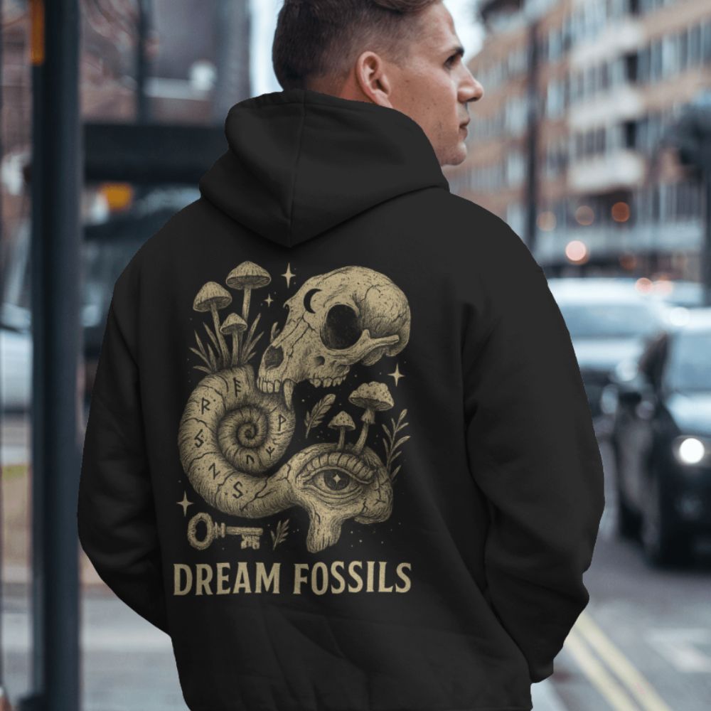Person wearing a black “Dream Fossils” hoodie showing a skull and snail illustration on the back, photographed in an urban streetwear environment