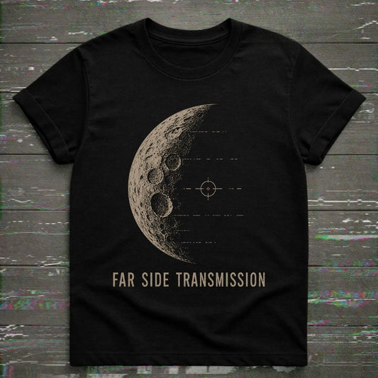 A black short-sleeve crewneck t-shirt featuring a distressed beige graphic of the moon's far side with a target symbol and the text 'FAR SIDE TRANSMISSION' printed below, displayed flat on a dark wood plank background.