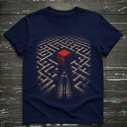 A navy blue short-sleeve t-shirt with a graphic print of a person standing in a maze looking up at a red cube, laid flat on a dark wood background.