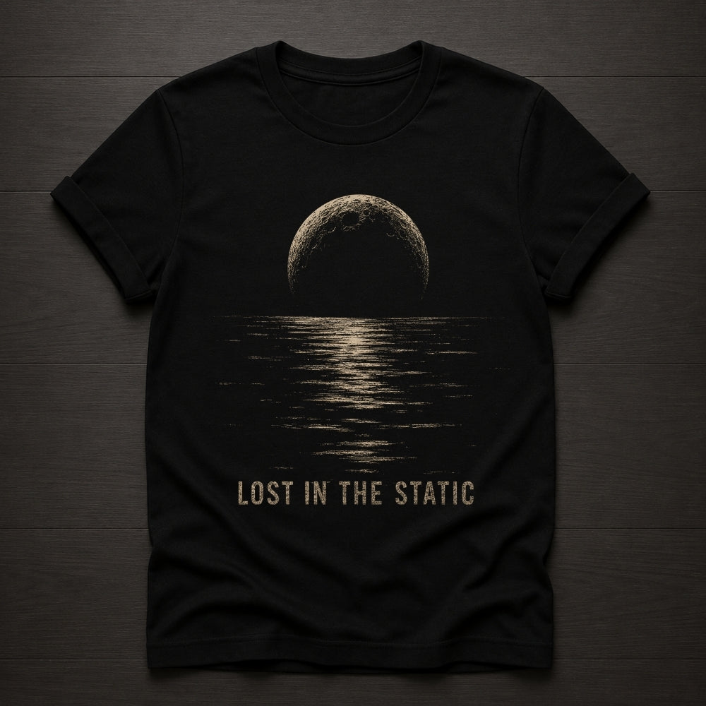 A black short-sleeve t-shirt laid flat on a dark wood background, featuring a distressed beige graphic of a moon over water with the text 'LOST IN THE STATIC' printed below.