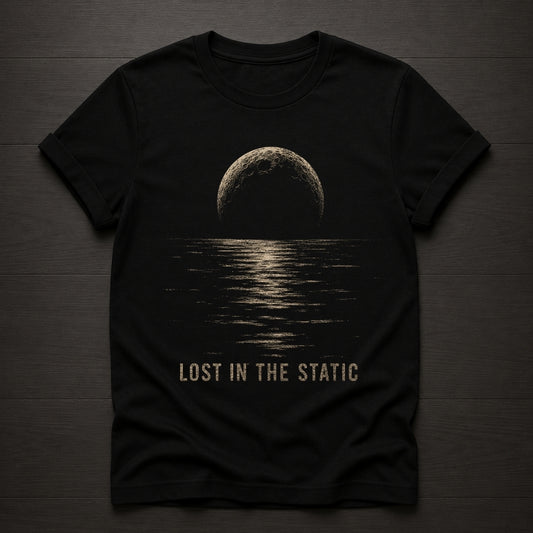 A black short-sleeve t-shirt laid flat on a dark wood background, featuring a distressed beige graphic of a moon over water with the text 'LOST IN THE STATIC' printed below.