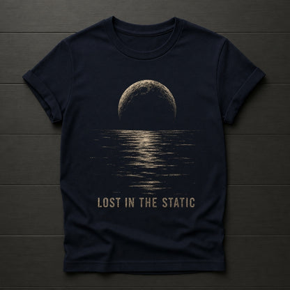A dark navy blue t-shirt laid flat on a dark wood plank background. The shirt features a graphic print of a half-moon reflecting light on water, with the text 'LOST IN THE STATIC' printed below in a distressed beige font.