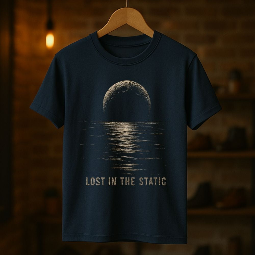 A navy blue short-sleeve t-shirt hanging on a wooden hanger against a warm, blurred brick wall background. The shirt features a graphic print of a moon over water with the text 'LOST IN THE STATIC' printed below in a distressed beige font.