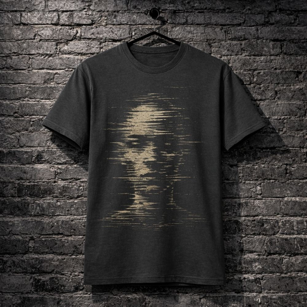 A dark charcoal gray t-shirt hanging on a black hanger against a dark gray brick wall. The shirt features a distressed, pixelated graphic of a face in a sandy beige color on the front.