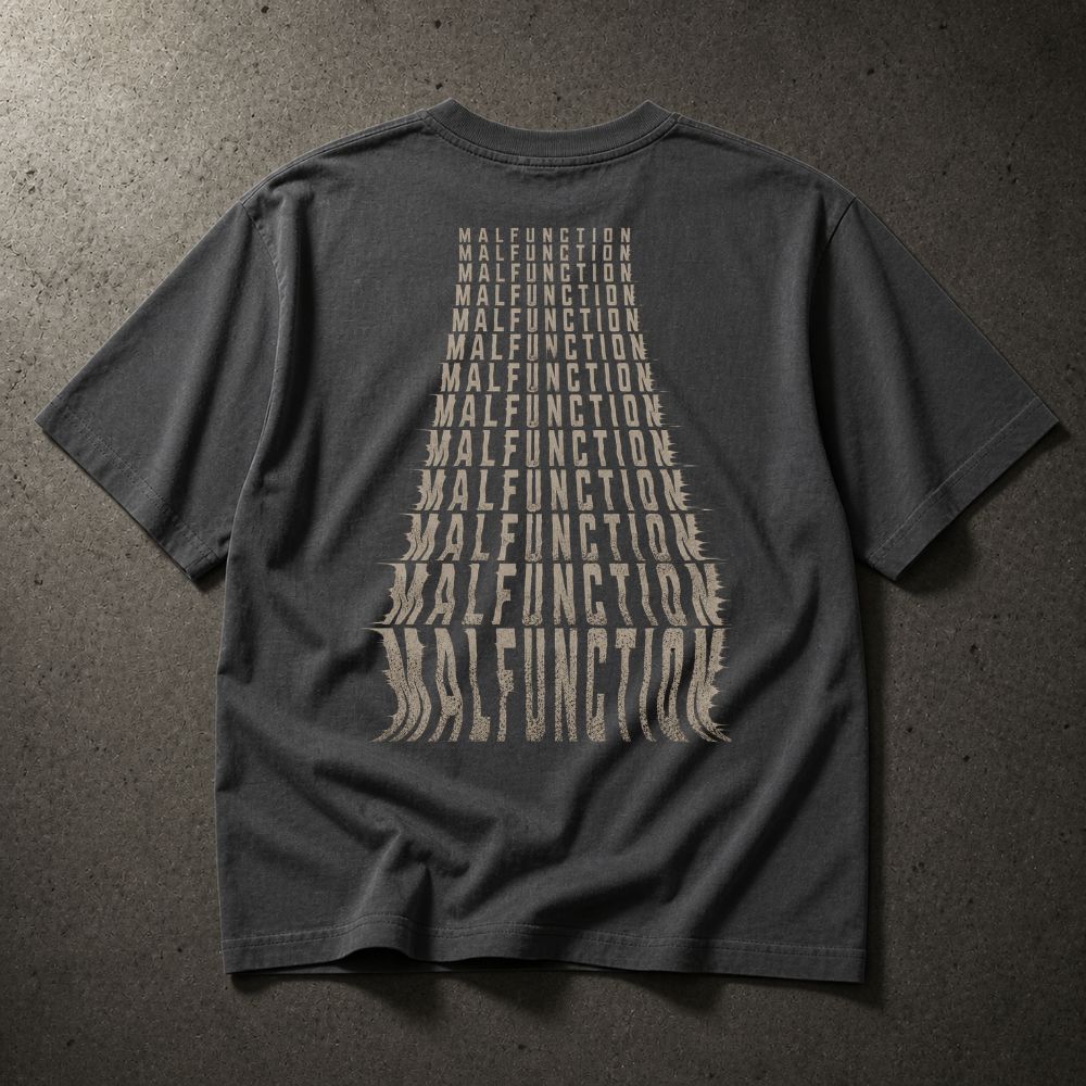 A dark gray t-shirt laid flat on a textured gray background, showing the back with a large beige graphic of the word 'MALFUNCTION' repeated in a converging triangle pattern.