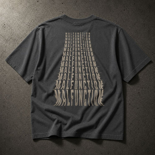 A dark gray t-shirt laid flat on a textured gray background, showing the back with a large beige graphic of the word 'MALFUNCTION' repeated in a converging triangle pattern.