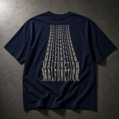 A navy blue short-sleeve t-shirt laid flat on a textured gray concrete surface, featuring a large graphic print on the back in a light beige color that spells out 'MALFUNCTION' in a tapered, layered font.