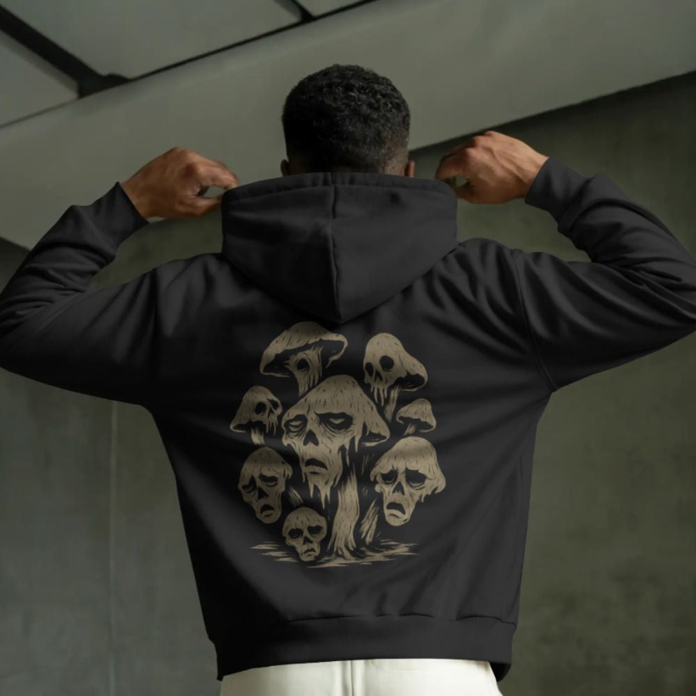 Model wearing a black hoodie with a surreal mushroom skull design on the back, dark streetwear aesthetic.