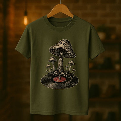 An olive green short-sleeve t-shirt hanging on a wooden hanger against a warm, blurred brick wall background. The shirt features a detailed graphic print of a mushroom growing on a vinyl record.