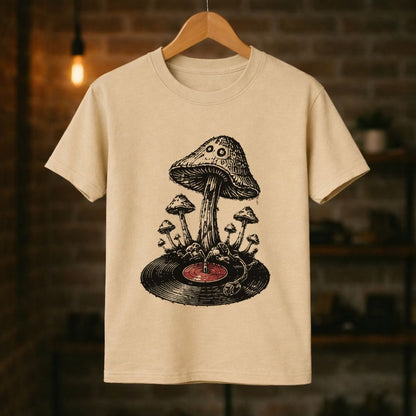 A cream-colored short-sleeve t-shirt hanging on a wooden hanger against a blurred brick wall background. The shirt features a detailed black ink-style graphic of a mushroom growing from a vinyl record with a small red center.