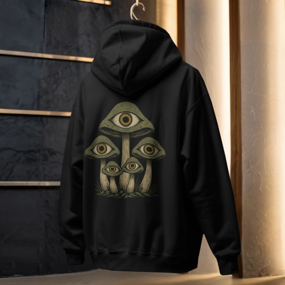 Black hoodie with surreal mushroom illustration featuring eye motifs on the back, displayed on a hanger in a modern studio setting.