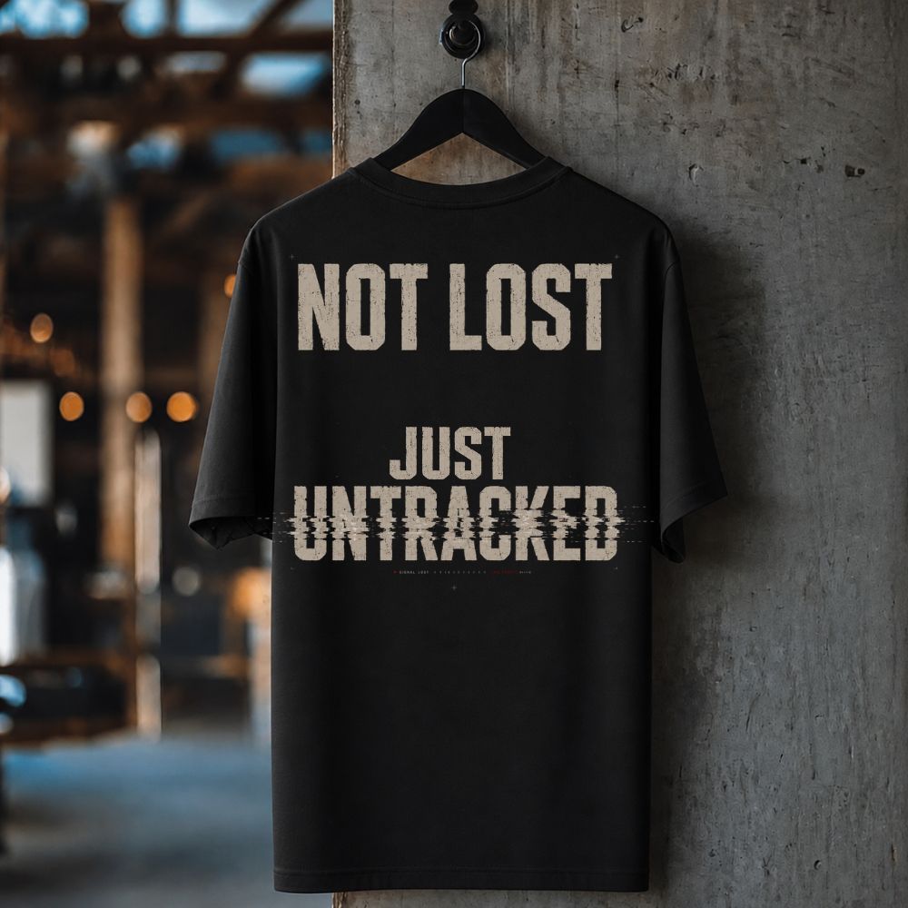A black short-sleeve t-shirt hanging on a black hanger against a textured concrete pillar, featuring the distressed beige text 'NOT LOST JUST UNTRACKED' on the back.