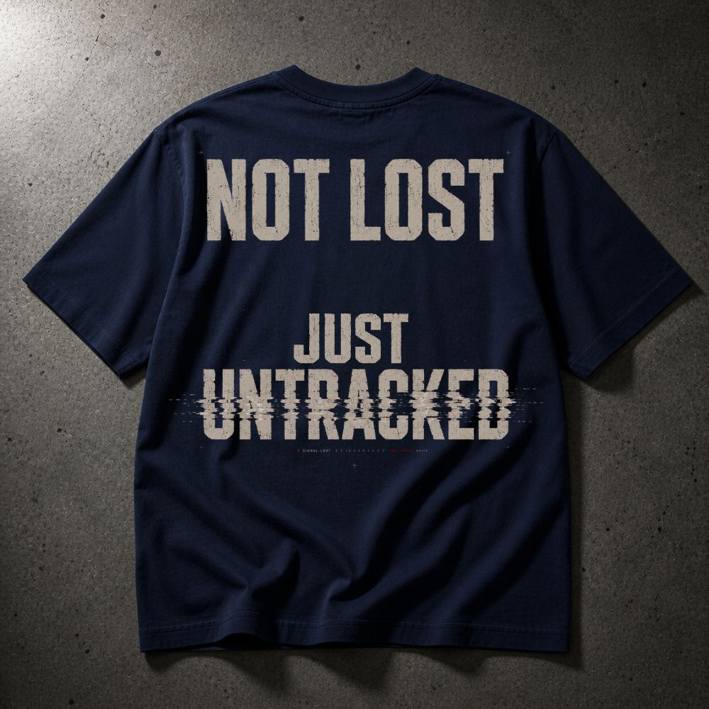 A navy blue t-shirt with the phrase 'NOT LOST JUST UNTRACKED' printed in distressed off-white text across the back, laid flat on a textured gray concrete surface.