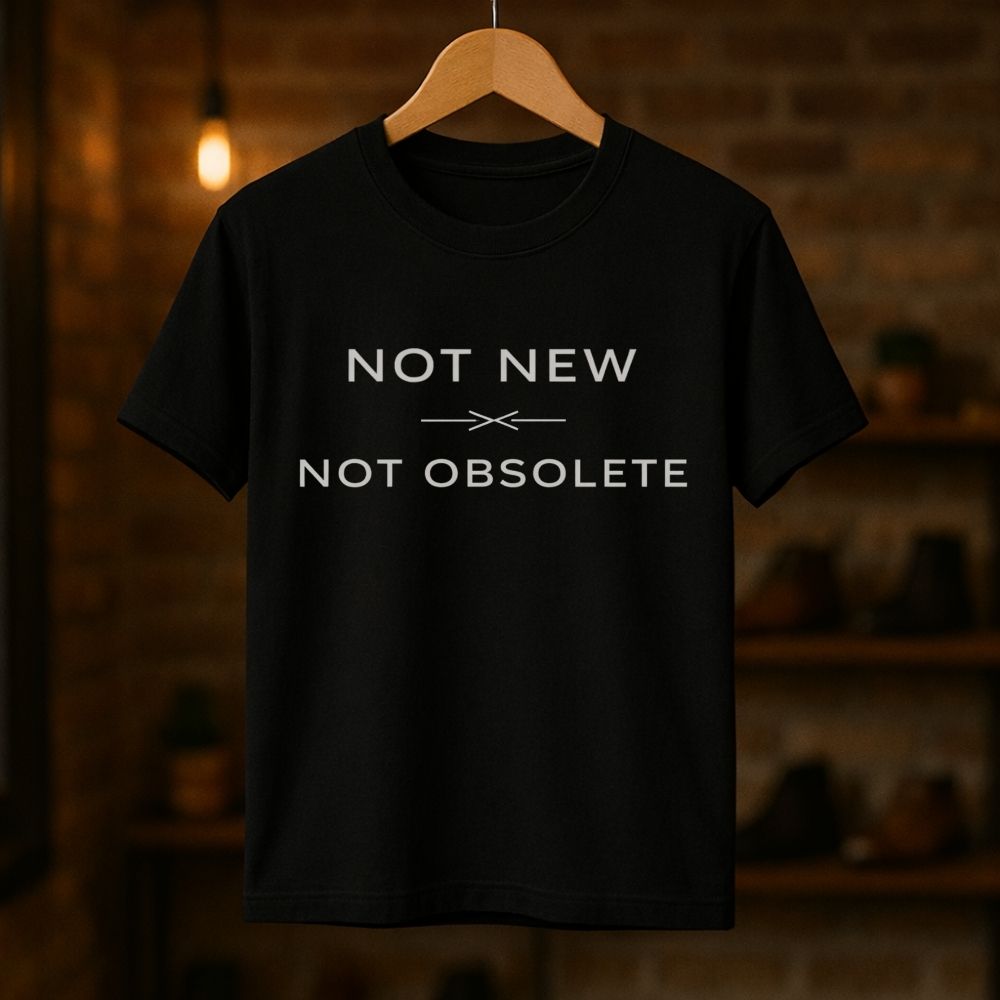 Black t-shirt with 'Not New Not Obsolete' text on a wooden hanger against a dark background