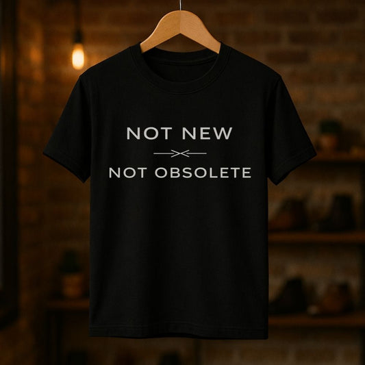 Black t-shirt with 'Not New Not Obsolete' text on a wooden hanger against a dark background