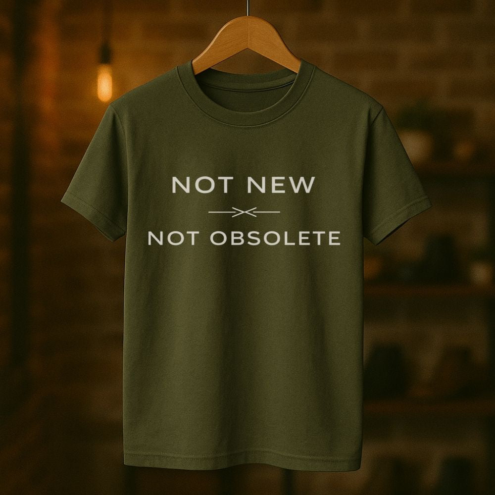 Green t-shirt with 'Not New Not Obsolete' text on a wooden hanger against a blurred background