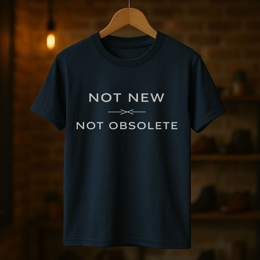 Navy blue t-shirt with 'Not New, Not Obsolete' text on a wooden hanger against a dark background.
